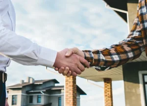 Using Hard Money Loans in New York to Finance Multi-Family Properties 3 handshake in front of a property, symbolizing a real estate deal or financial agreement.