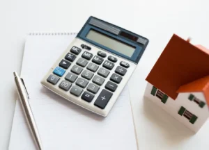 How DSCR Loans Help Real Estate Investors Scale Their Portfolios 2 Calculator next to a model house representing calculation of net operating income for real estate investment