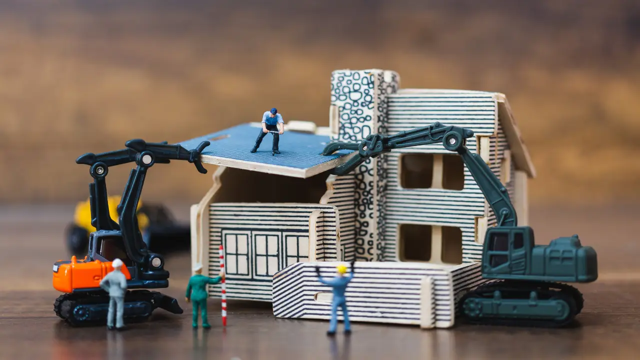 Miniature people working on building a home, representing home renovation and fix and flip loan projects for real estate investors